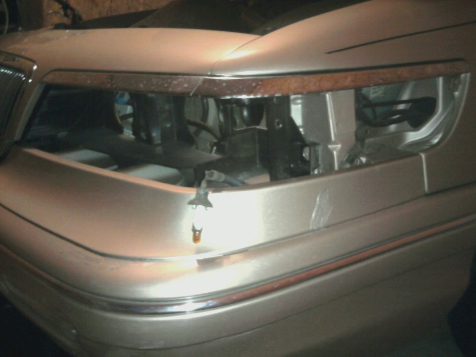 Tan car front end with chrome trim and woodgrain accent above headlight opening