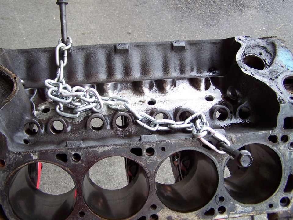 Bare V8 engine block with lifting chain bolted on, four cylinder bores exposed