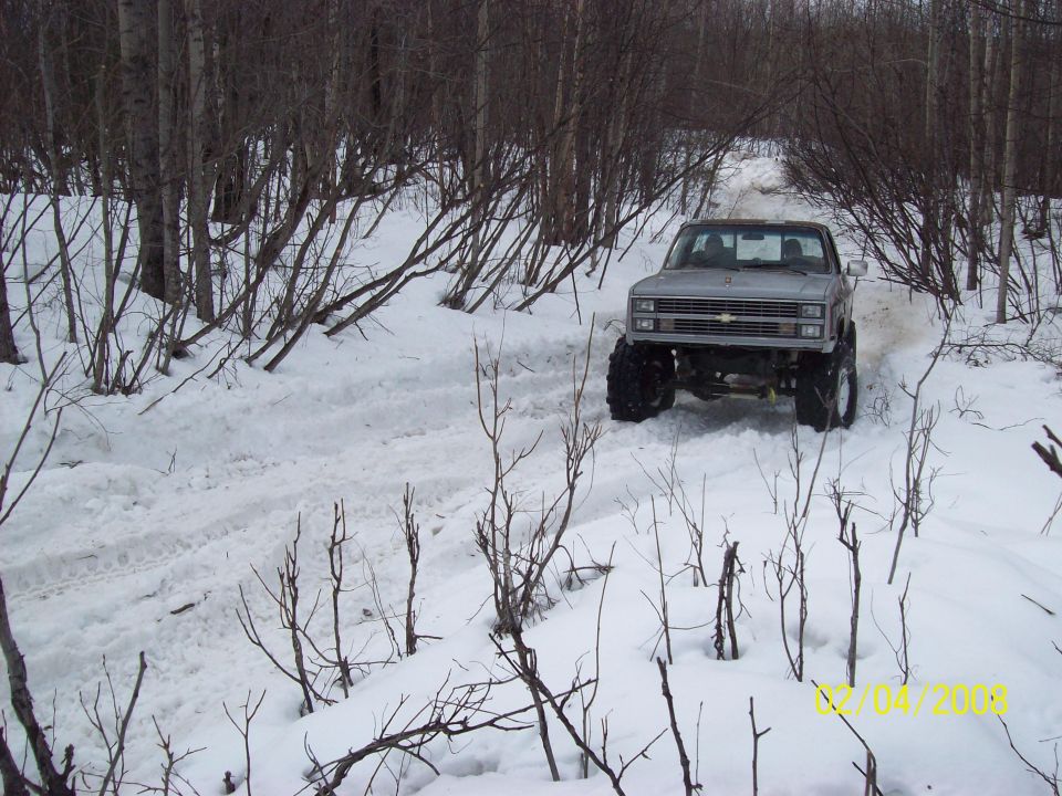 Silver pickup truck with large tires on a snowy path, front view