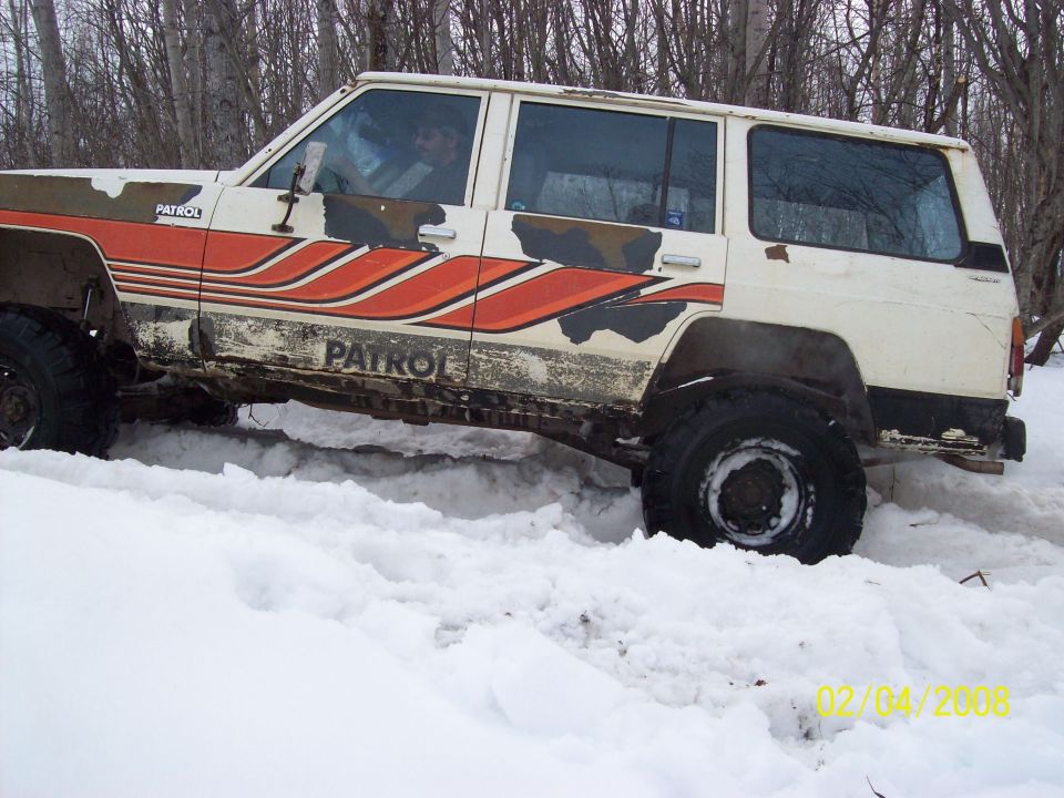 Nissan Patrol SUV driving through deep snow, showing side profile with 'PATROL' decals