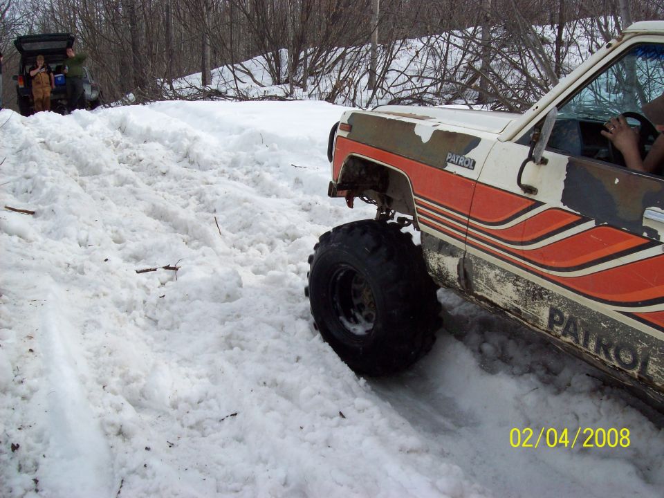Off-road vehicle with 'PATROL' on the side driving through deep snow. Another vehicle is visible in the background
