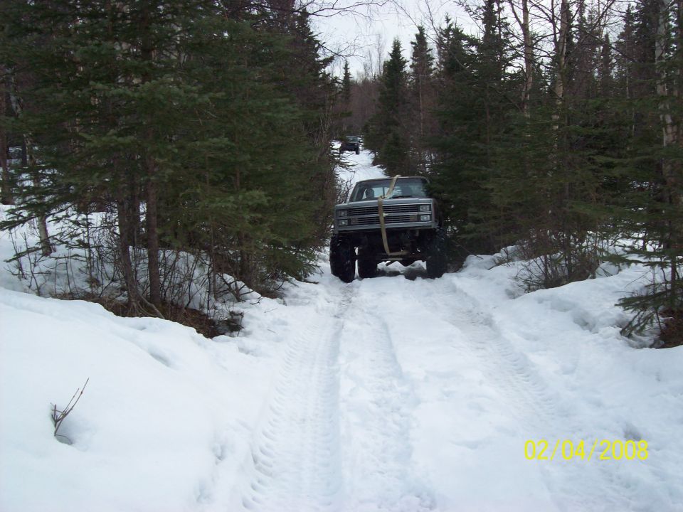 Lifted 1979 Chevrolet K5 Blazer driving on a snow-covered forest road with another vehicle behind it