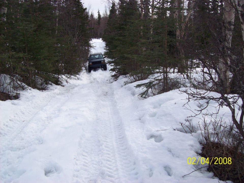 Dark SUV driving up a snowy road between trees