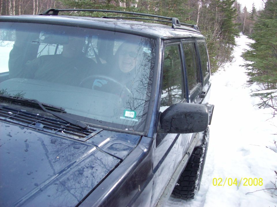 Dark SUV parked on a snowy path, driver visible through windshield