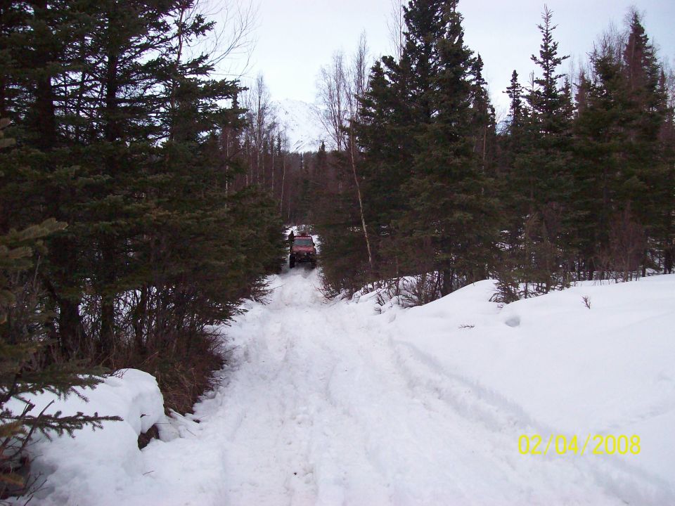 Off-road vehicle driving up a snow-covered path through a forest
