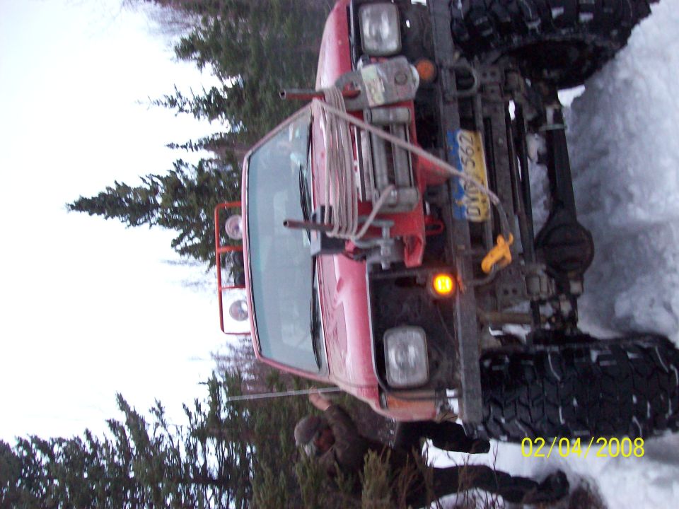 Red truck with tracks in snow, front view. Winch and yellow tow hook visible