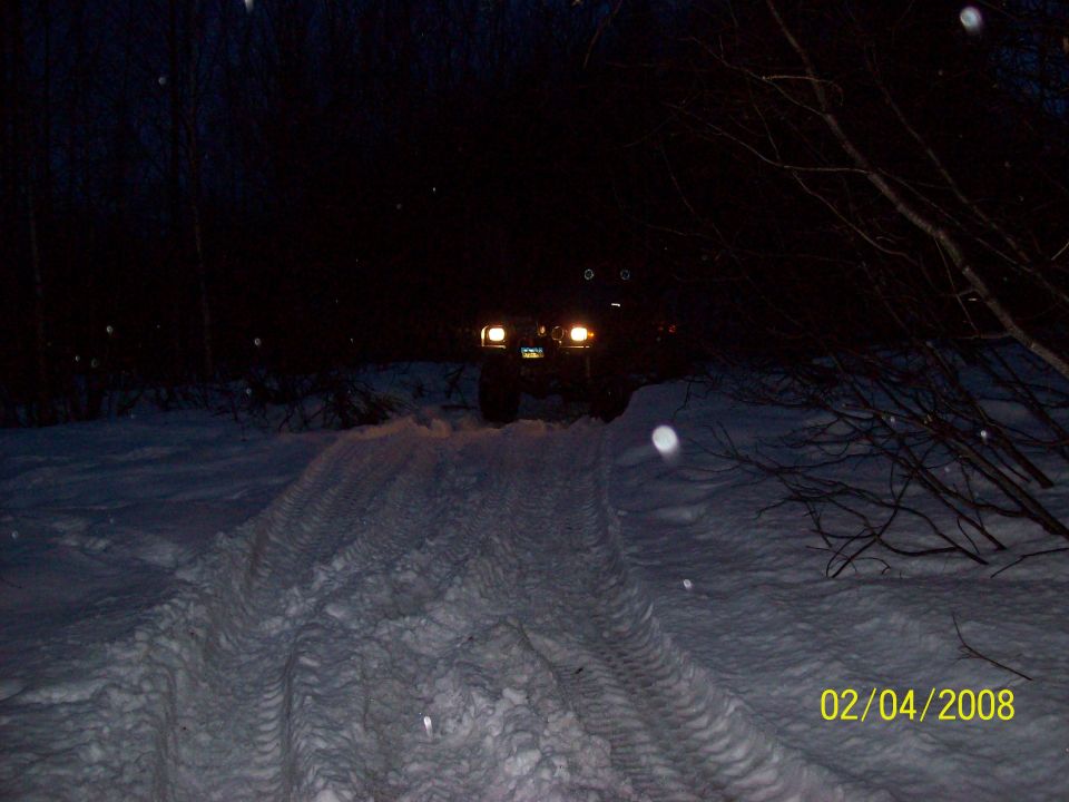 SUV driving in snow at night, headlights on