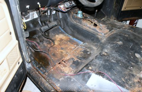 1979 Ford Bronco - The interior floor of a vehicle shows significant rust damage and exposed wiring.