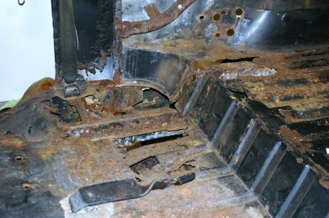 1979 Ford Bronco - The interior floor pan of a vehicle shows extensive rust damage and holes.