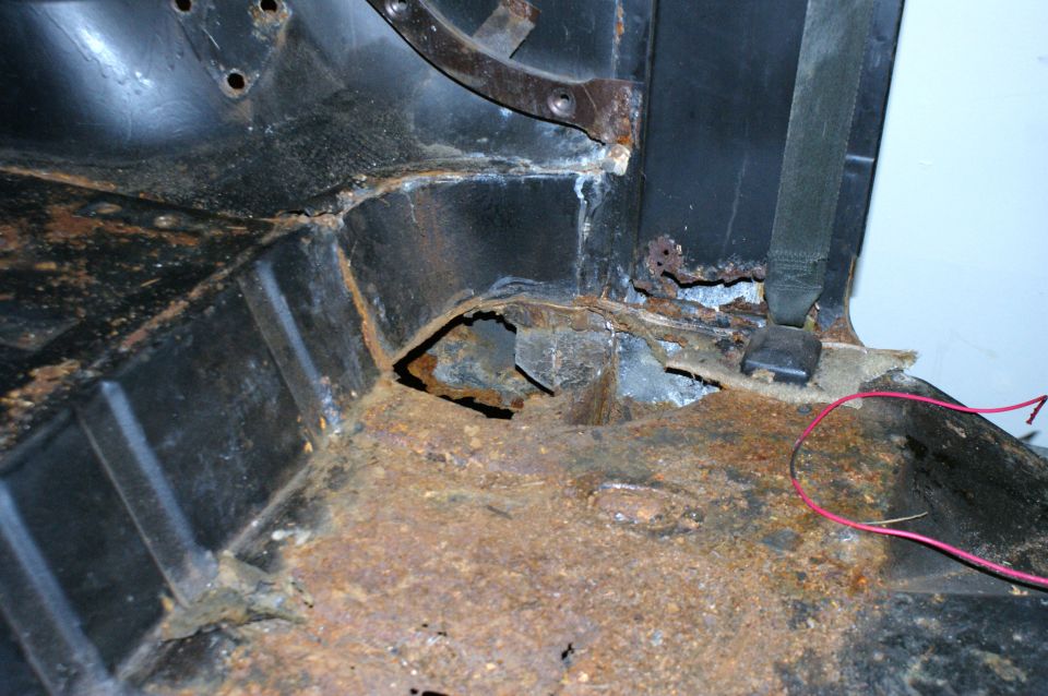Rusted interior floor pan with seatbelt anchor