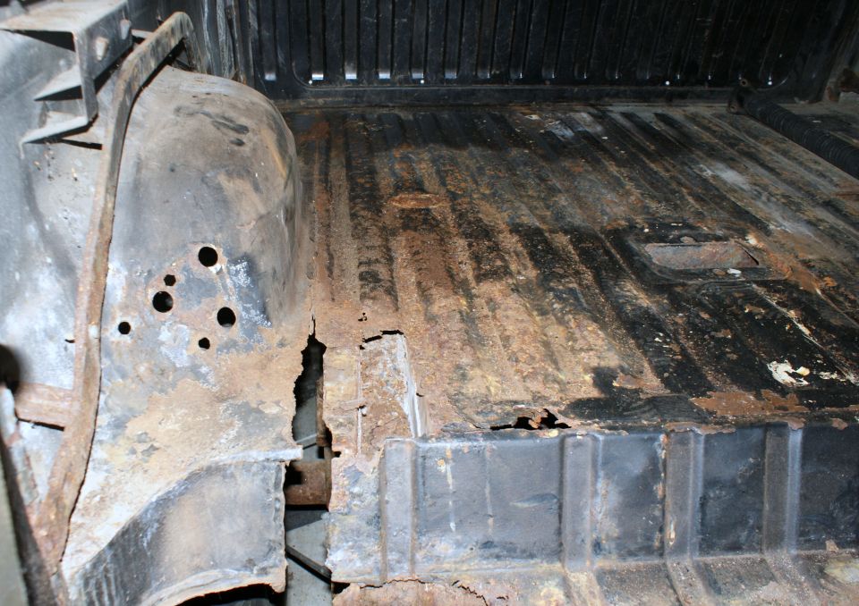 Interior of a rusty vehicle showing floor damage and wheel well