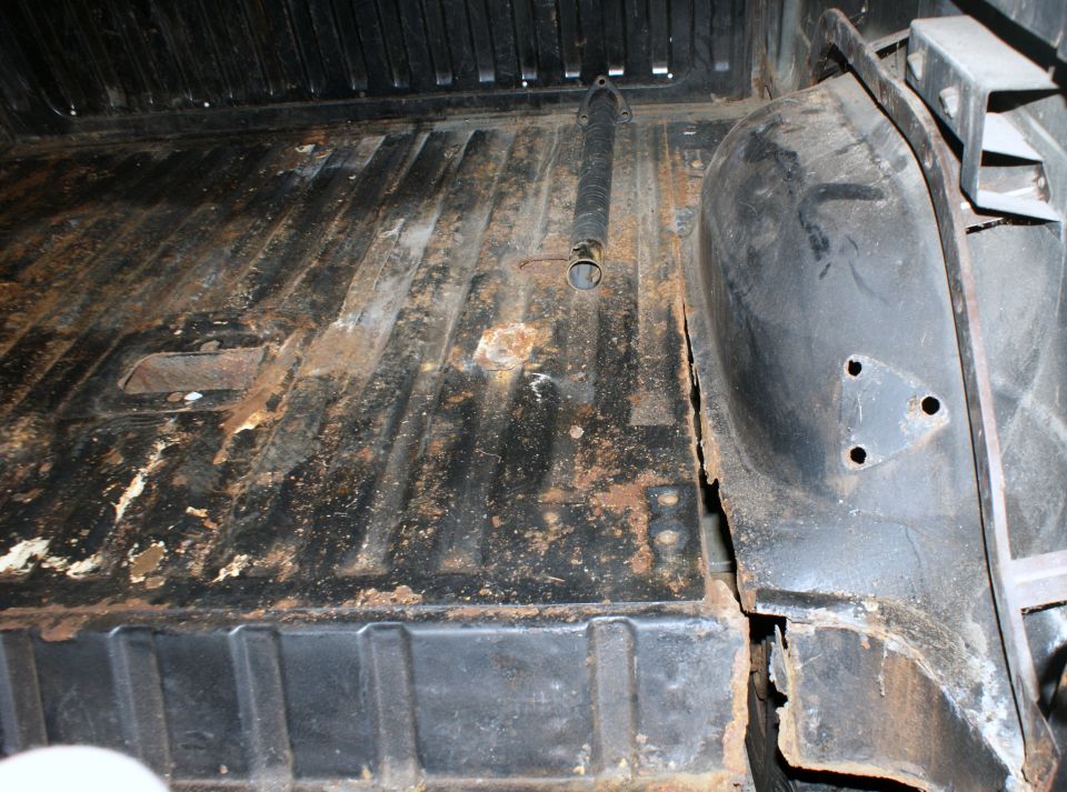 Interior cargo area of a vehicle showing rust and wear on the floor and wheel well