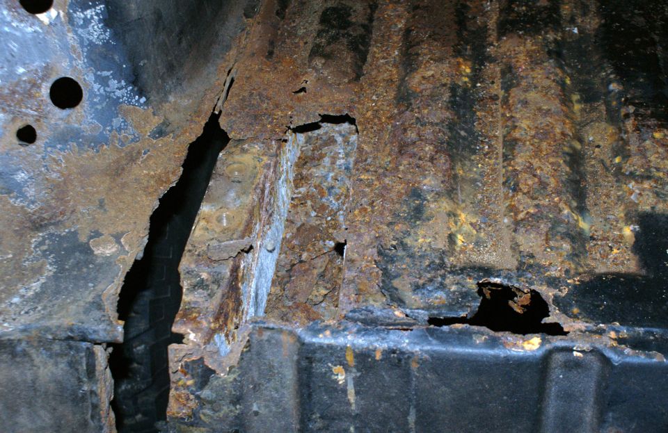 Vehicle interior floor with extensive rust and holes, showing structural damage