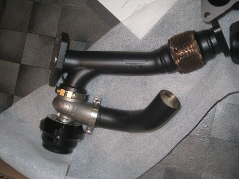 2007 Subaru Impreza - Close-up view of a turbocharger wastegate assembly, a black and silver finish and connected to an exhaust manifold with braided heat wrap.