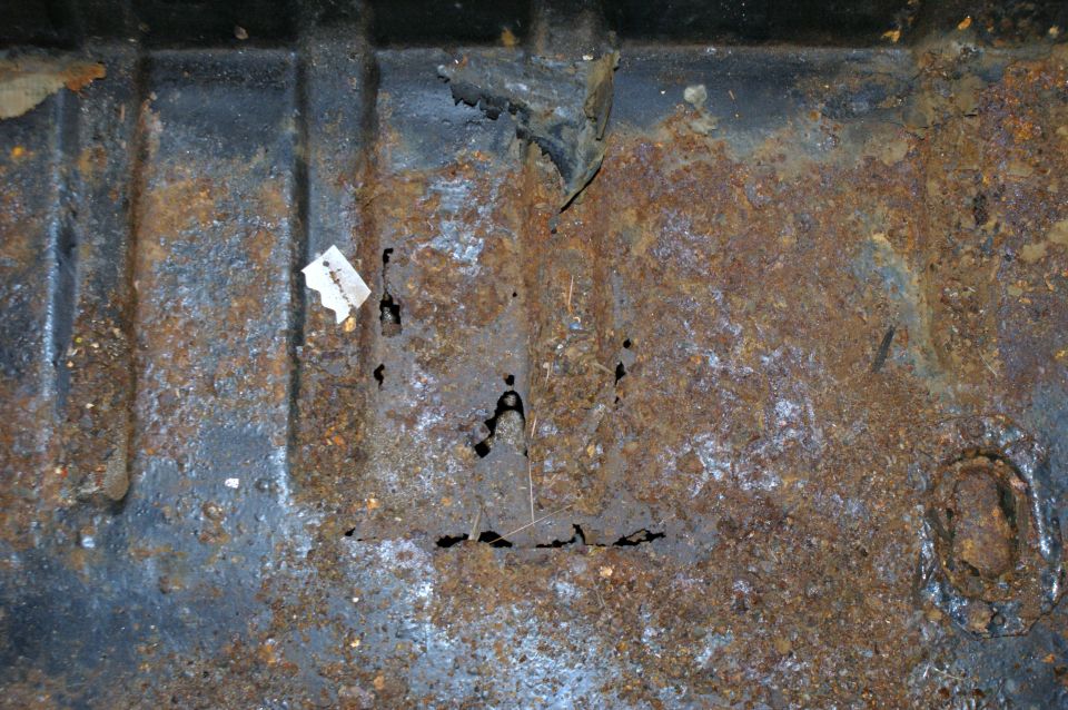 rusted metal floor pan with holes and a small piece of paper stuck to it