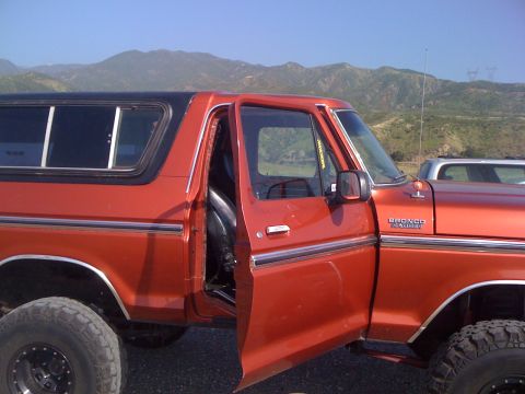 1978 Ford Bronco - Side view of an orange 1978 Ford Bronco with the driver's door ajar, parked outdoors.