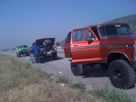 1978 Ford Bronco - Several vehicles are pulled over on the side of the road, with people attending to one of the Broncos.