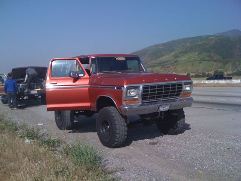 1978 Ford Bronco - A lifted 1978 Ford Bronco is parked on the side of the road with its door open, while another vehicle is being worked on nearby.