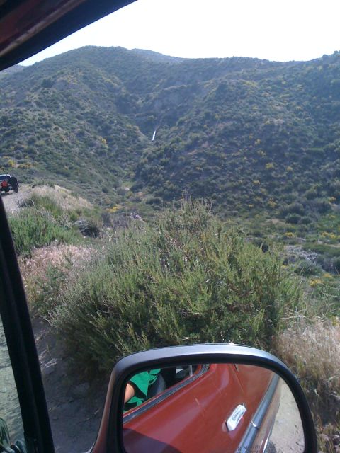 1978 Ford Bronco - Two vehicles navigate a steep, brush-covered mountain trail under a bright sky.