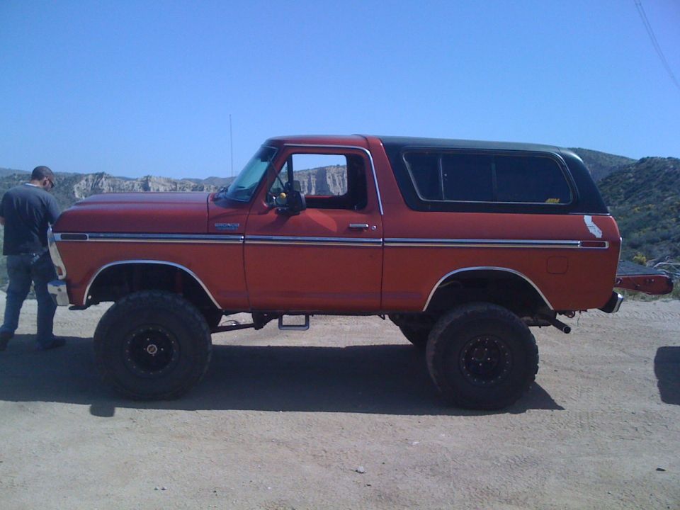 Red 1978 Ford Bronco side view with black top and large tires