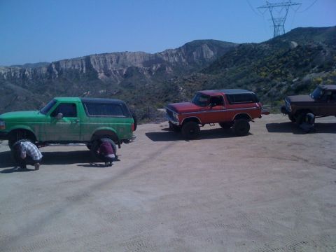 1978 Ford Bronco - Three Ford Broncos are parked on a dirt road with a mountainous landscape behind them.