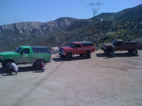 1978 Ford Bronco - A group of vehicles are parked in a dusty, outdoor area with a power line tower visible on the hill.