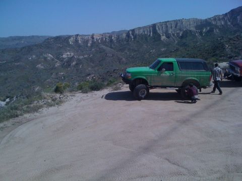 1978 Ford Bronco - A green SUV with a lifted suspension is parked on a dirt road with a mountainous landscape in the background.