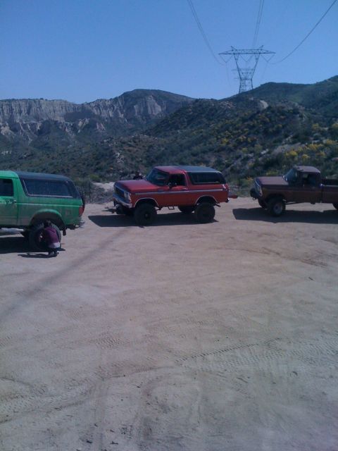 1978 Ford Bronco - A red 1978 Ford Bronco is parked alongside two trucks in a dusty, mountainous area.