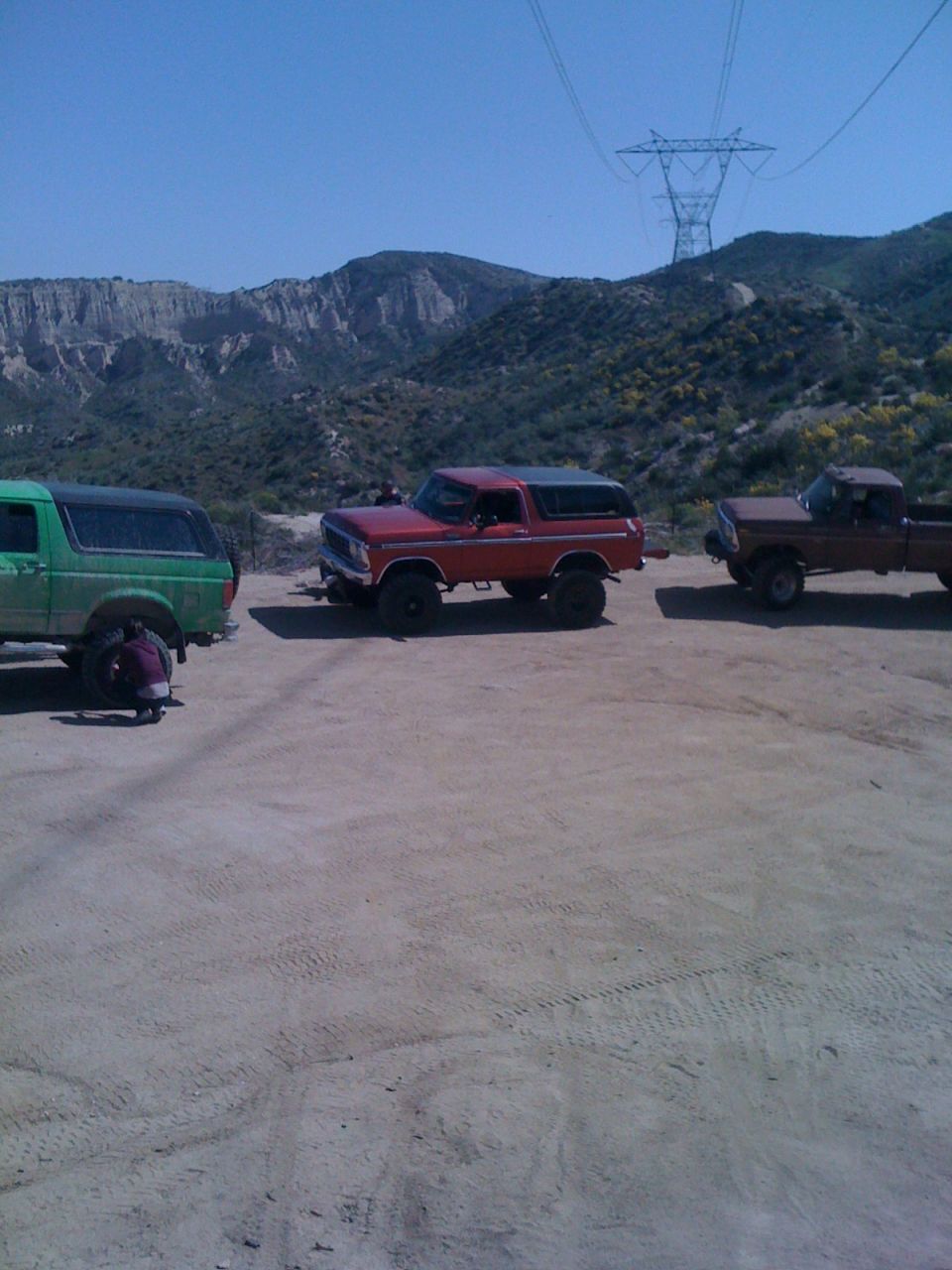 Red 1978 Ford Bronco 3q-front view with two trucks in a desert landscape