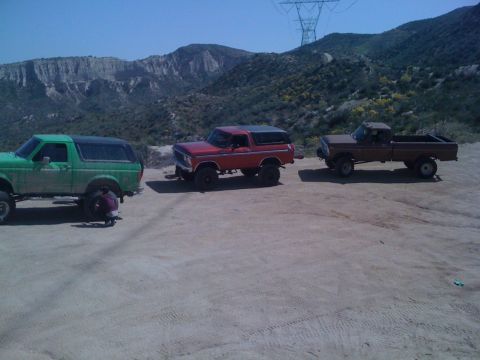 1978 Ford Bronco - Three Ford vehicles, including two Broncos and a pickup truck, are parked on a dirt road in a mountainous area.