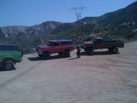 1978 Ford Bronco - Three off-road vehicles are parked on a dirt road in a hilly, arid landscape under a clear blue sky.