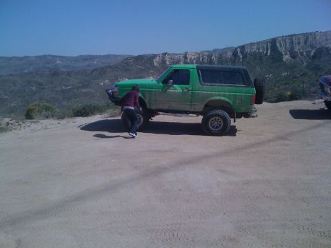 1978 Ford Bronco - A green SUV is parked on a dirt road with a person standing next to it, overlooking a mountainous landscape.