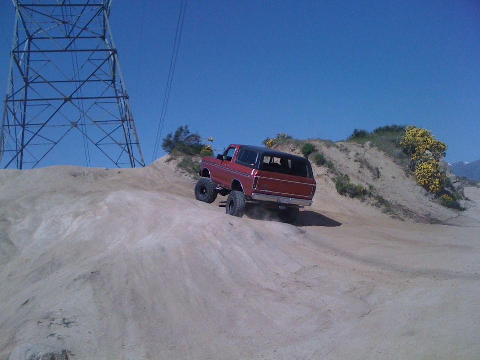 Red 1978 Ford Bronco climbing a sandy hill with a power tower in the background