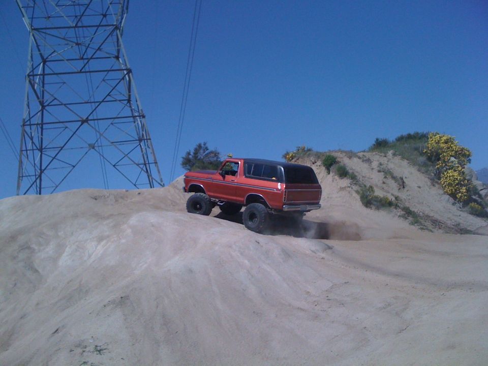 Orange Ford Bronco climbing a dirt hill near a power tower