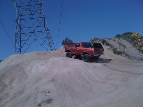 1978 Ford Bronco - A red 1978 Ford Bronco navigates a sandy incline under a clear blue sky.