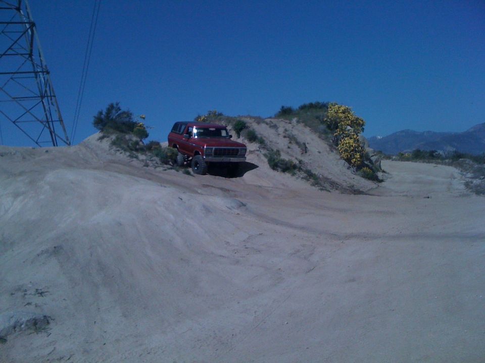 Red 1978 Ford Bronco driving off-road on a sandy hill