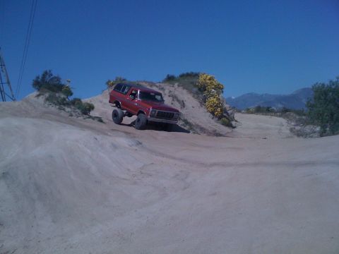 1978 Ford Bronco - A red 1978 Ford Bronco navigates a sandy incline under a clear blue sky.