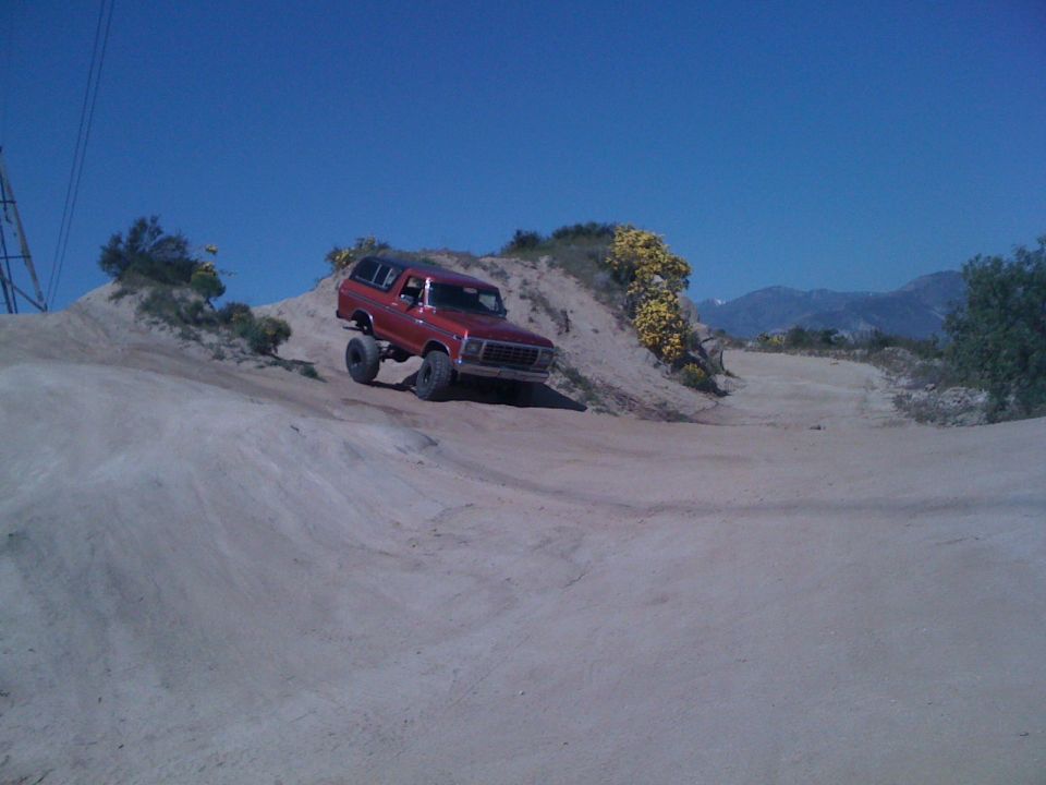 Red 1978 Ford Bronco driving on a dirt hill with yellow flowers