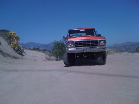 1978 Ford Bronco - An orange Ford truck is parked on a dirt road with hills in the background.