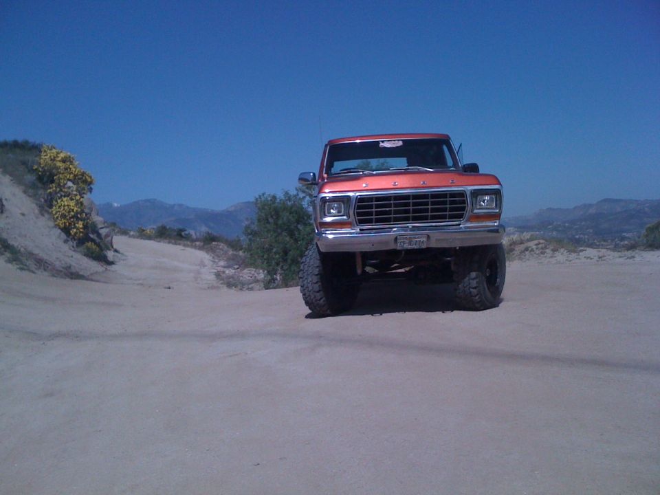 Orange Ford truck with lifted suspension and large tires parked on a dirt road