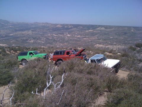 1978 Ford Bronco - Three SUVs, including a 1978 Ford Bronco, are parked on a dirt trail in a hilly, arid landscape.