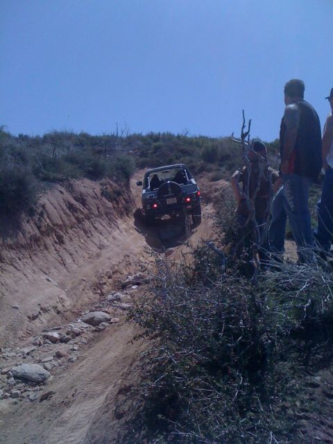 1978 Ford Bronco - A dark SUV navigates a challenging off-road trail with onlookers observing the action.