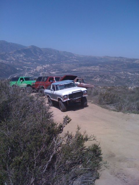 1978 Ford Bronco - Several off-road vehicles, including a silver Ford pickup, are parked on a dirt path with mountains in the background.