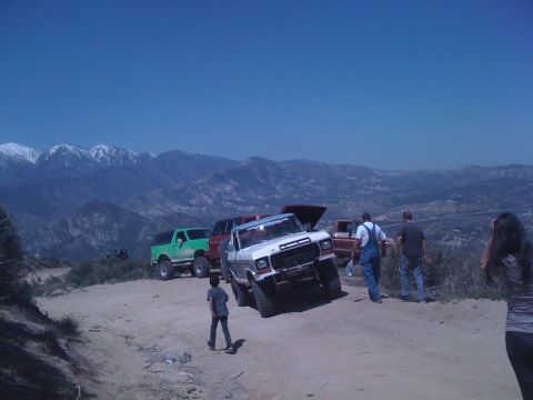 1978 Ford Bronco - Several off-road vehicles are gathered on a dirt path with a mountainous landscape behind them.