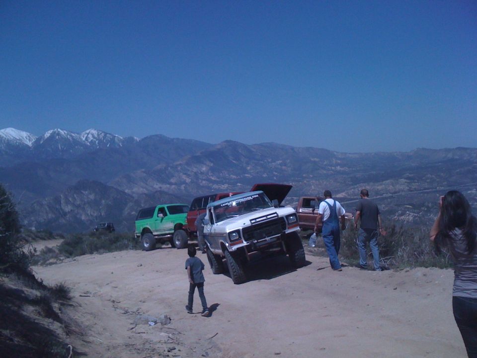 White pickup truck with hood open, 3q-front view, on a dirt road with mountains in background