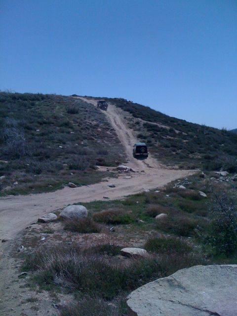 1978 Ford Bronco - Two SUVs ascend a challenging dirt path on a dry, grassy slope, with one vehicle ahead of the other.