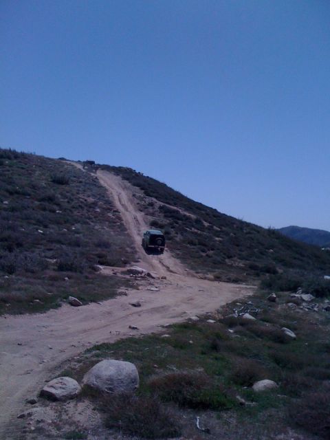 1978 Ford Bronco - A dark SUV navigates a challenging dirt path on a barren hillside under a clear blue sky.