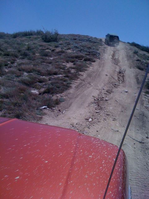 1978 Ford Bronco - Two vehicles navigate a steep, dusty dirt road on a hillside under a clear blue sky.