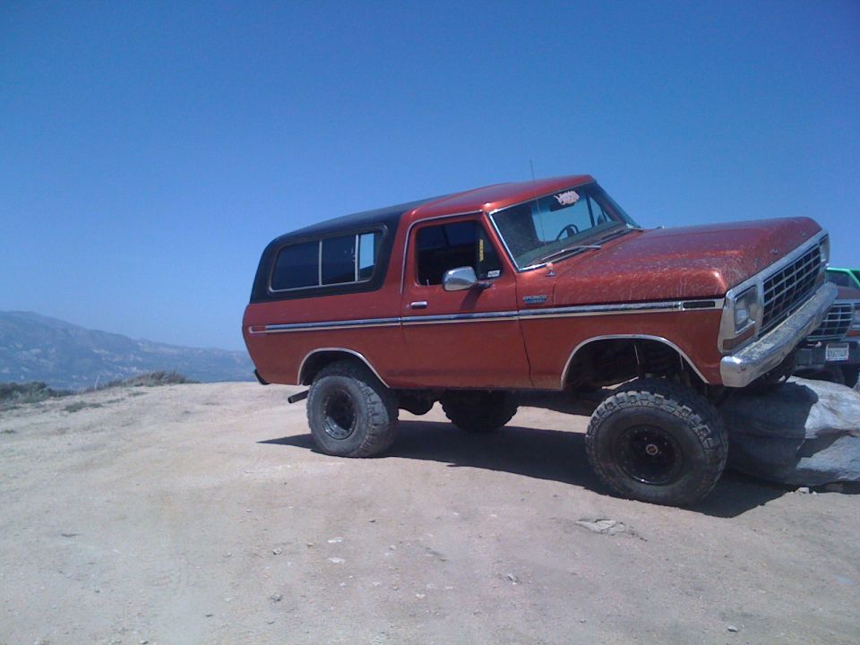 Orange 1978 Ford Bronco on rocks, another vehicle behind it