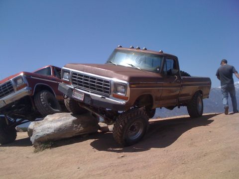 1978 Ford Bronco - Two lifted pickup trucks navigate rocky terrain under a clear blue sky.